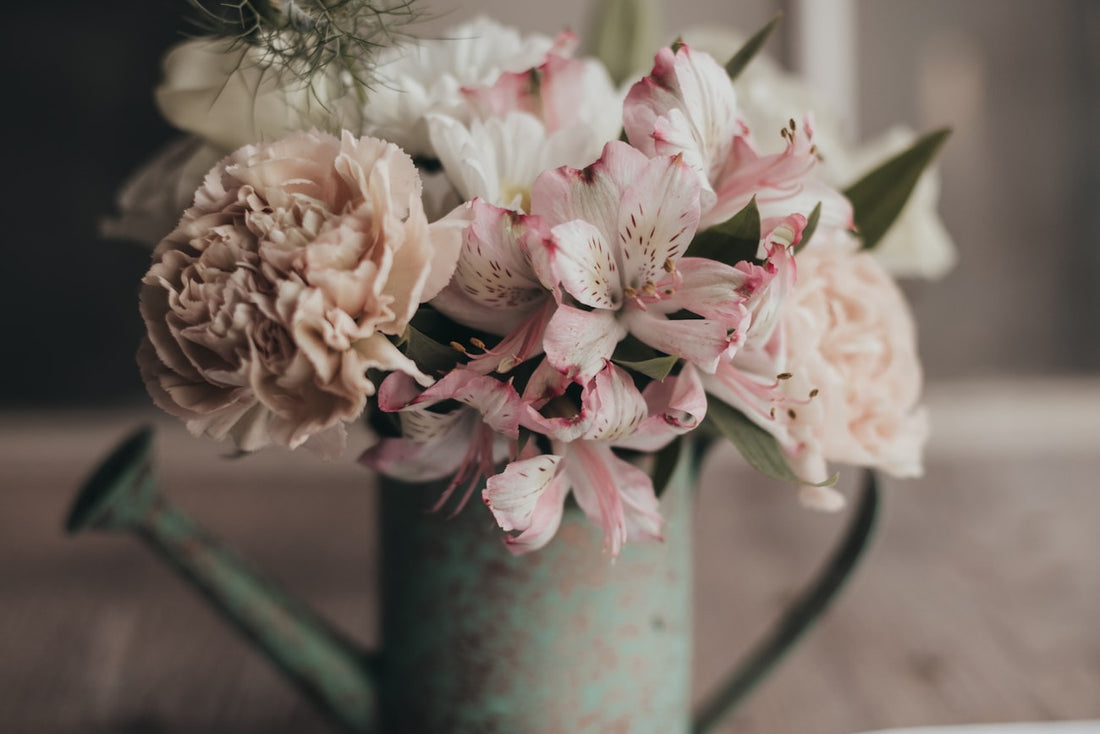Gießkanne mit Blumen neben einem offenen Tagebuch – ein Gartentagebuch führen